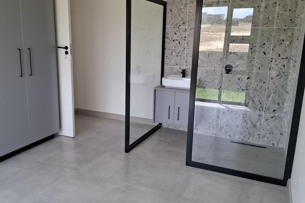 Modern bedroom featuring an open-plan en-suite bathroom with a glass shower enclosure, vanity unit, and contemporary grey floor tiling.