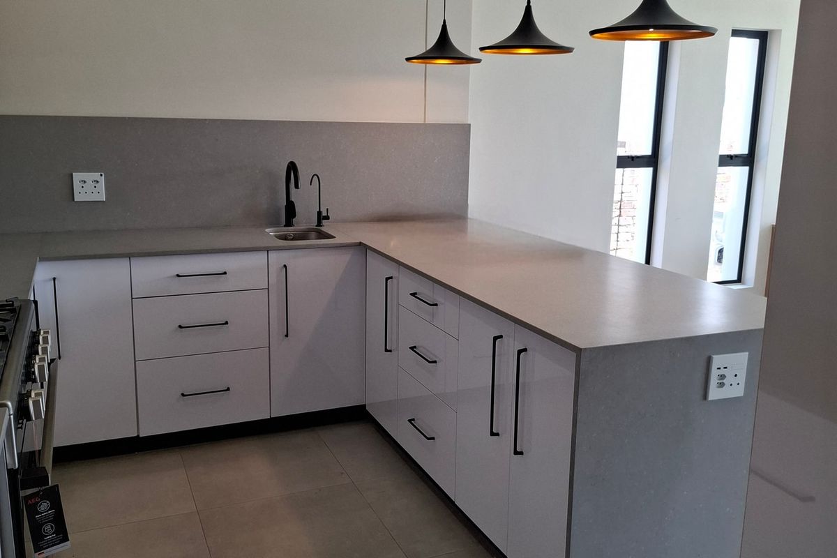 Modern kitchen featuring sleek white cabinetry, grey quartz countertops, tiled flooring, and contemporary pendant lighting in a clean, minimalist design.