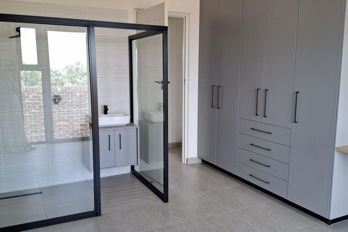 Modern bedroom featuring extensive built-in grey cabinetry and an integrated glass-enclosed shower area with a sleek vanity and basin.