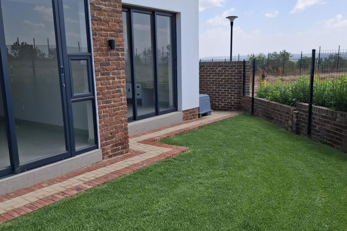 A well-maintained rear garden featuring a manicured lawn, brick boundary walls, and modern aluminium sliding doors leading into the home.