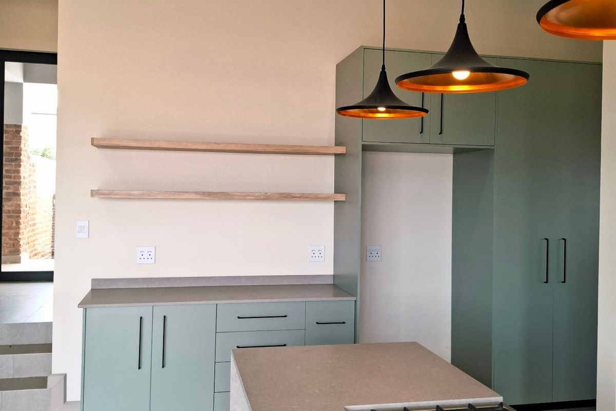 Modern kitchen featuring sage green cabinetry, stone countertops, a central island with a built-in gas cooktop, and contemporary pendant lighting.