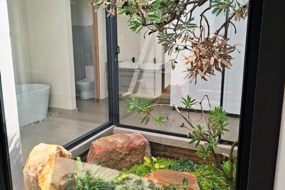 Modern bathroom featuring a central glass-enclosed atrium with natural landscaping, a freestanding bathtub, and a double vanity with contemporary finishes.