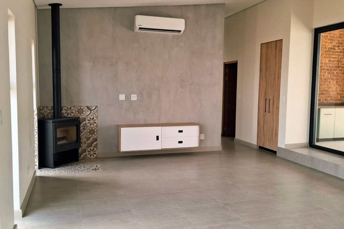 Spacious living area featuring large format floor tiles, a modern freestanding fireplace with decorative tiling, and a wall-mounted air conditioning unit.