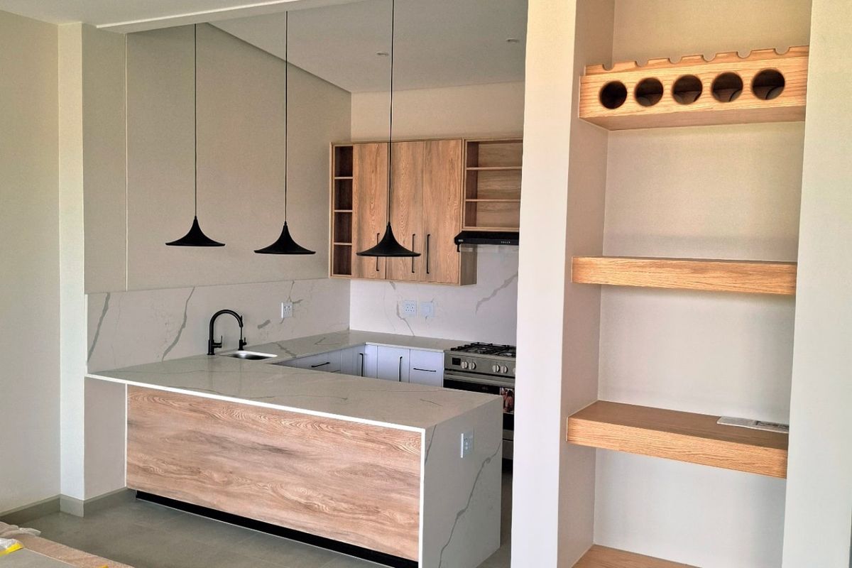 Modern kitchen featuring stone countertops, wood-finish cabinetry, built-in shelving, and integrated wine storage, complemented by sleek pendant lighting and high-quality finishes.