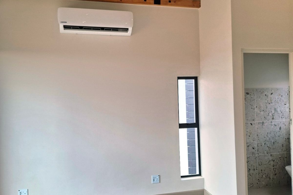 Spacious bedroom featuring high vaulted ceilings with exposed timber trusses, tiled flooring, split-system air conditioning, and an adjoining en-suite bathroom.