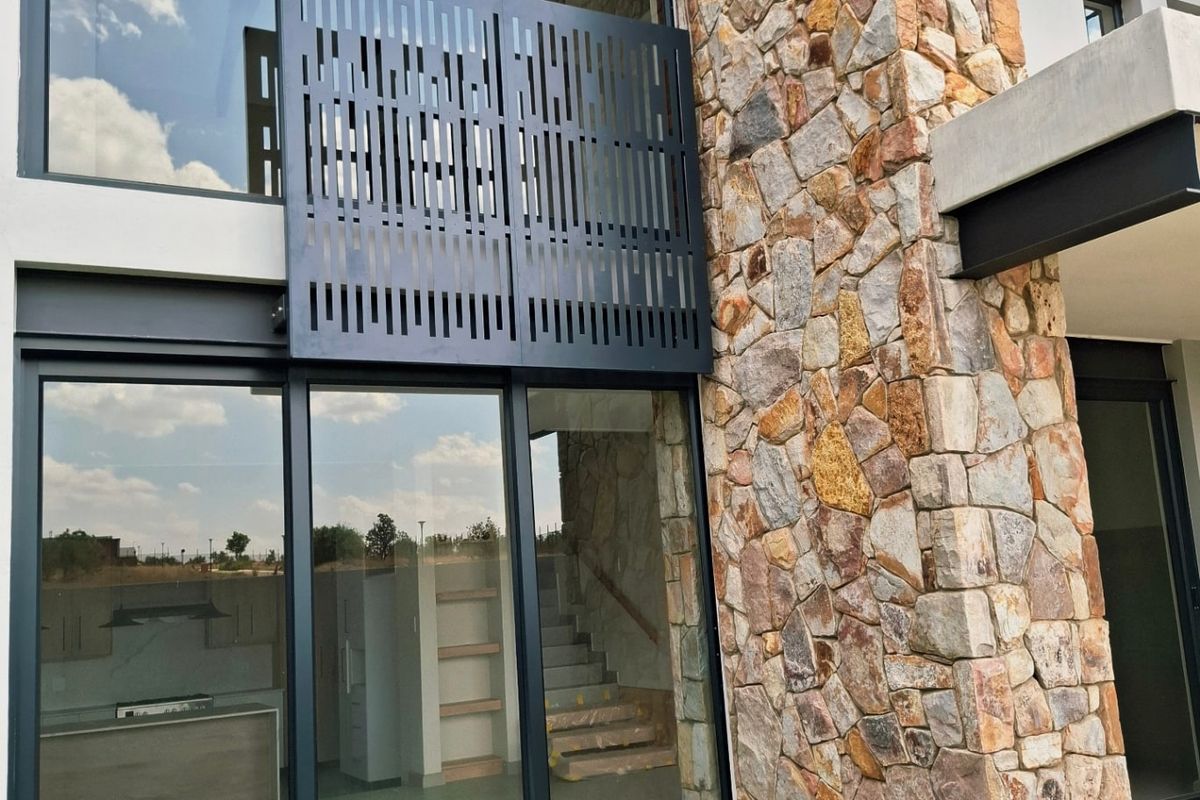 Modern rear facade featuring natural stone cladding, expansive floor-to-ceiling glass sliding doors, and a decorative metal privacy screen.