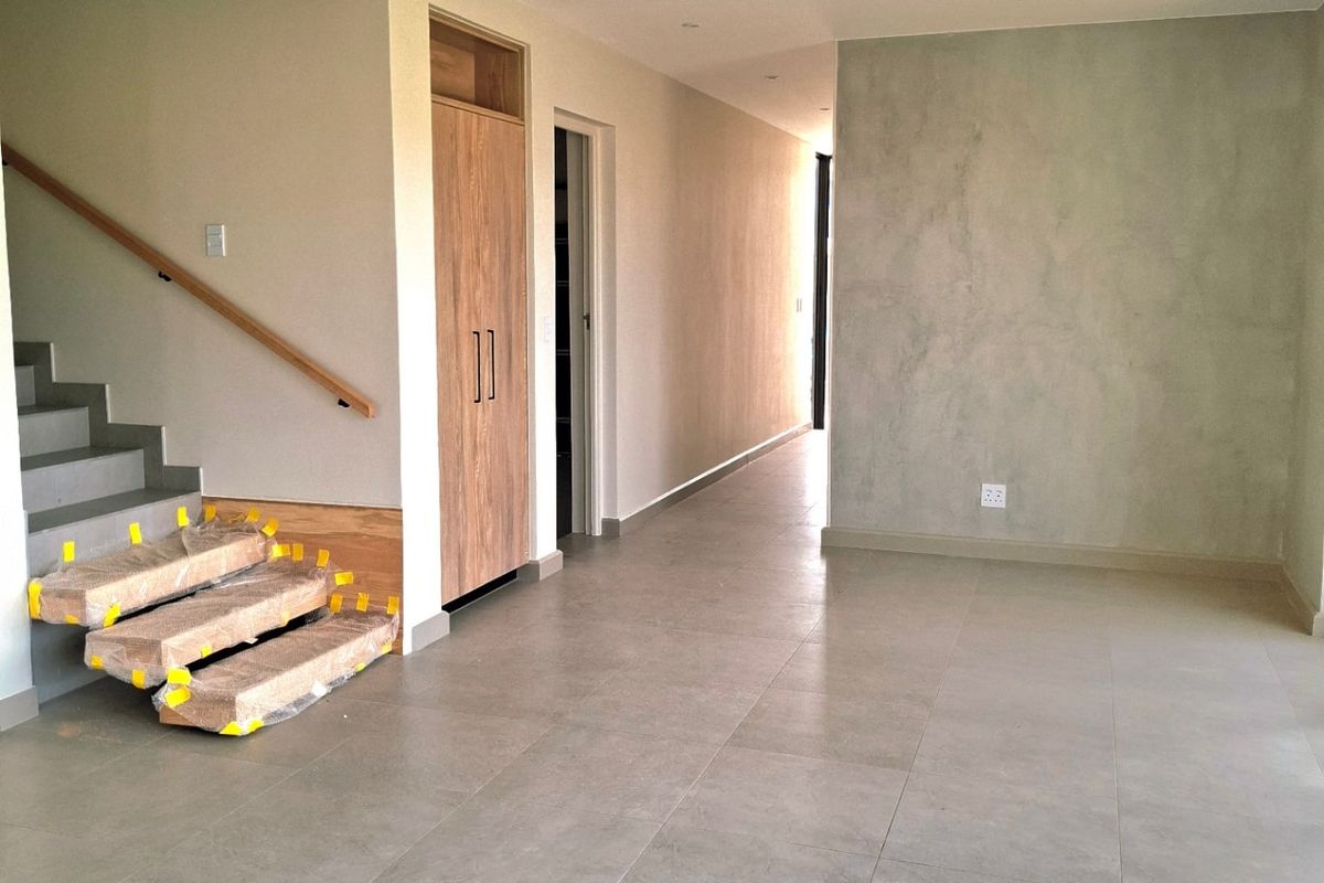 An open-plan living area featuring modern tiled flooring, recessed lighting, a built-in cupboard, and a staircase with a wooden handrail.