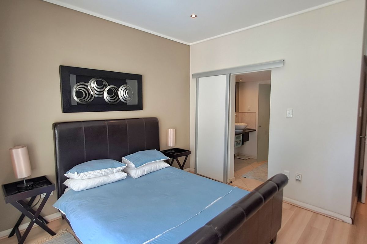 A well-maintained bedroom featuring laminate flooring, recessed downlighting, and an en-suite bathroom accessible via a sliding door.