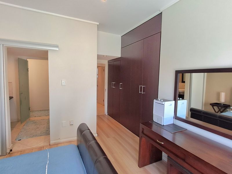 A well-maintained bedroom featuring dark wood built-in cupboards, laminate flooring, and recessed lighting, with an adjoining en-suite bathroom.