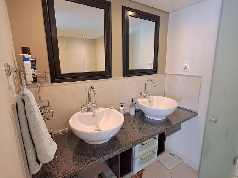 A modern bathroom featuring a double vanity with vessel sinks, granite countertops, and dual framed mirrors, providing a functional and stylish space.