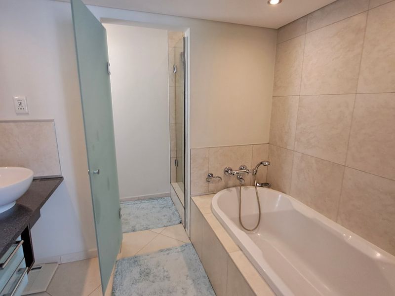 A modern bathroom featuring a built-in bathtub, tiled walls, a vanity with a vessel sink, and a separate shower enclosure.
