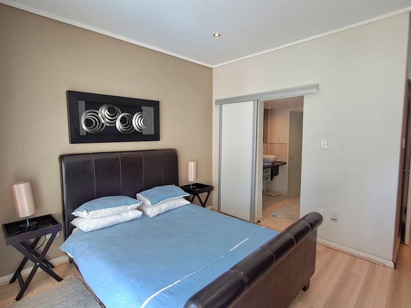 A well-maintained bedroom featuring laminate flooring, recessed downlighting, and an en-suite bathroom accessible via a sliding door.