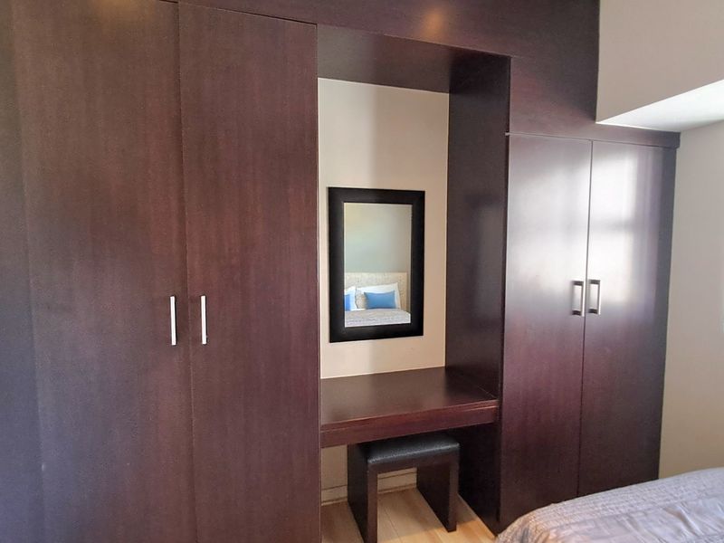 Bedroom featuring dark wood built-in wardrobes with an integrated vanity station and light-toned laminate flooring.