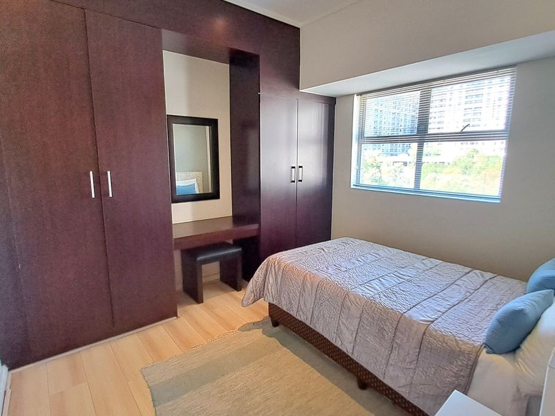 A well-maintained bedroom featuring extensive dark wood built-in cupboards with an integrated vanity area, laminate flooring, and large windows with blinds.
