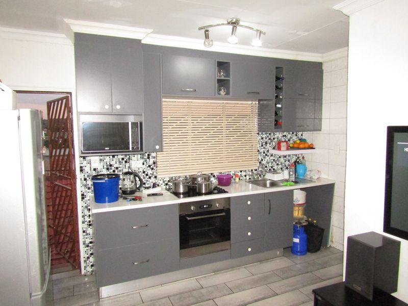 Modern kitchen featuring grey cabinetry, built-in oven and hob, mosaic tile backsplash, and stainless steel sink with tiled flooring.