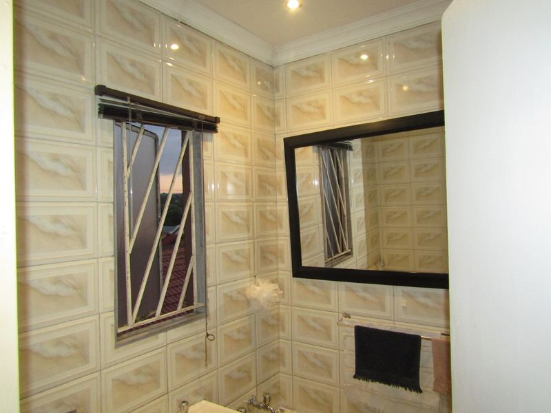 A functional bathroom featuring fully tiled walls, a wall-mounted mirror, and security bars on the window.