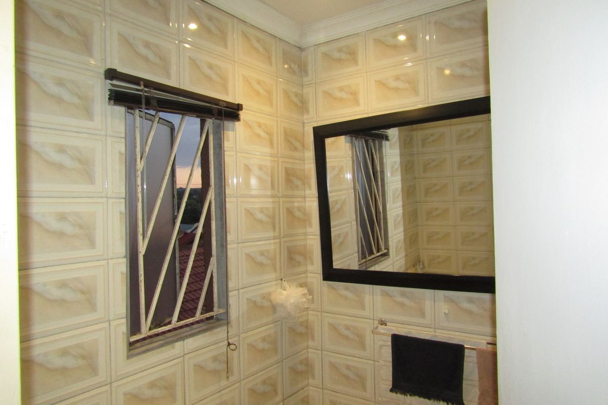 A functional bathroom featuring fully tiled walls, a wall-mounted mirror, and security bars on the window.