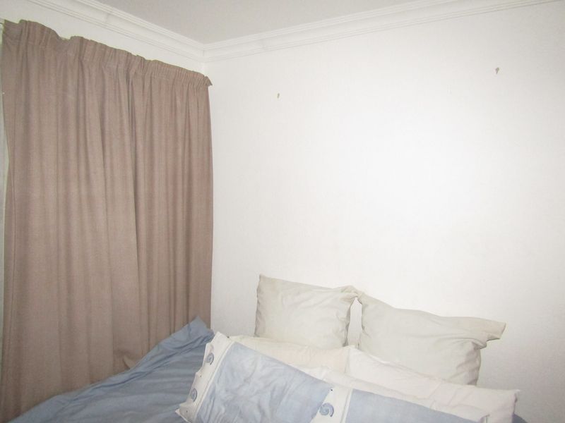 A simple bedroom interior featuring plain white walls and ceiling cornice.