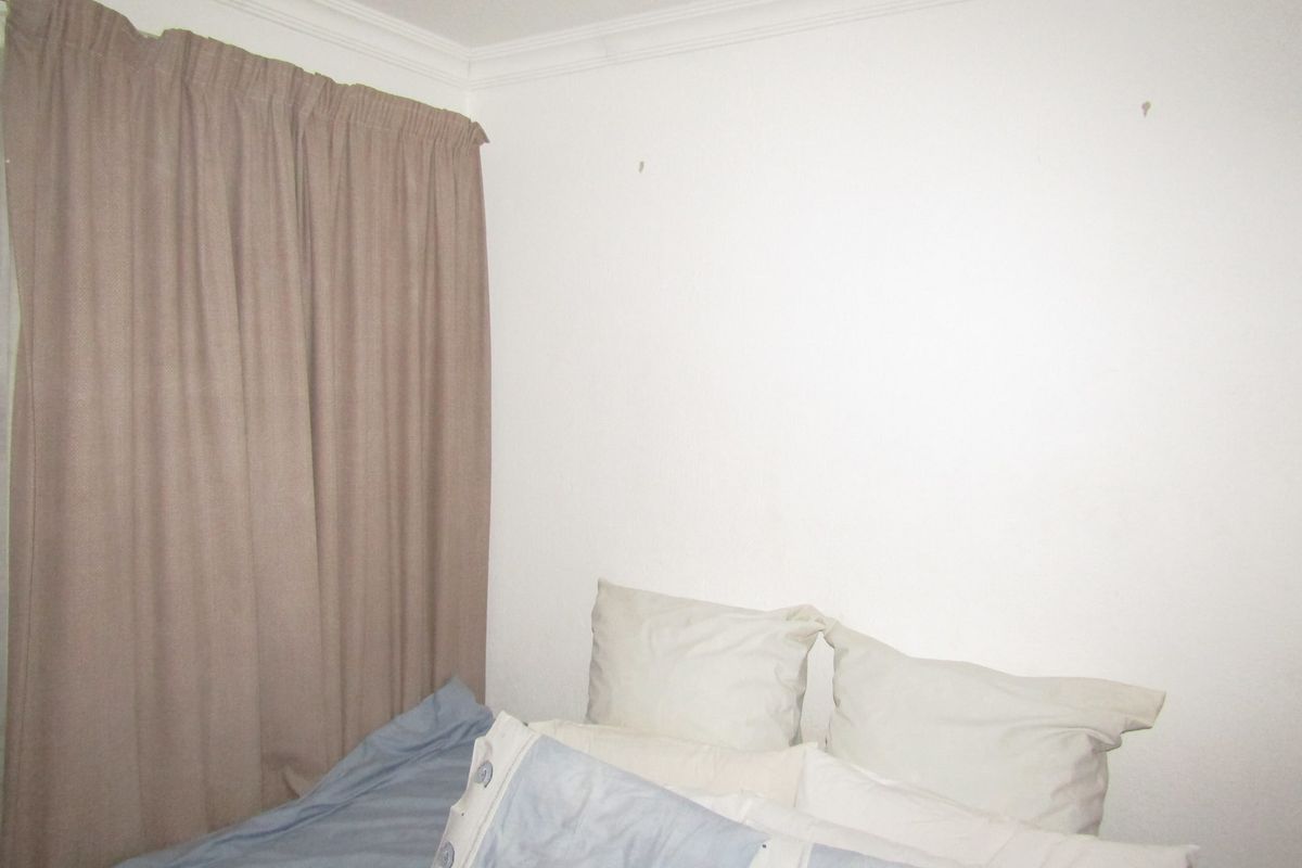 A simple bedroom interior featuring plain white walls and ceiling cornice.