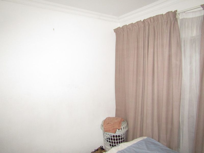 A corner view of a bedroom featuring plain white walls, decorative ceiling cornicing, and installed curtain tracks with curtains.