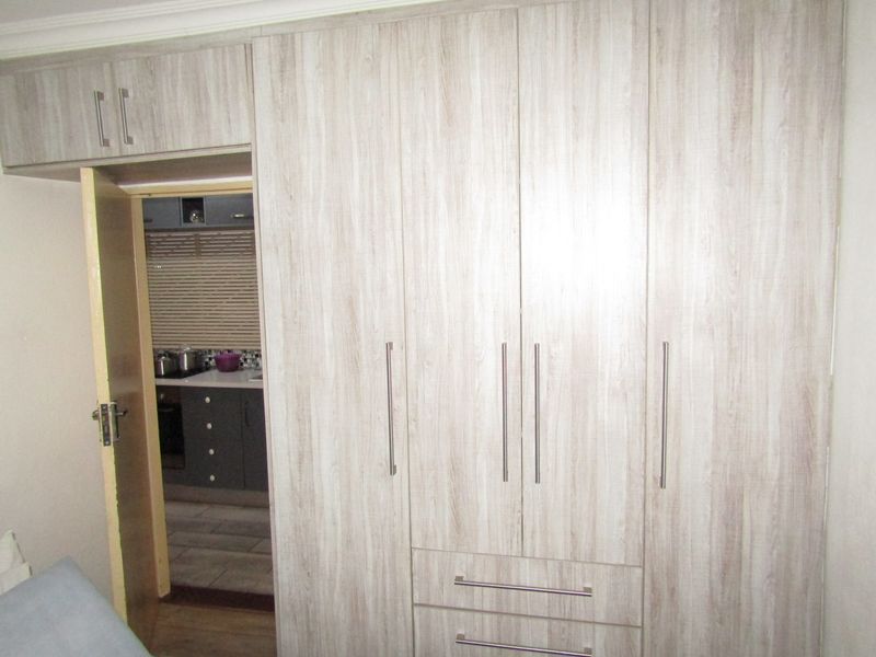 Bedroom featuring light wood-grain built-in wardrobes with integrated overhead storage and a doorway leading to the kitchen area.