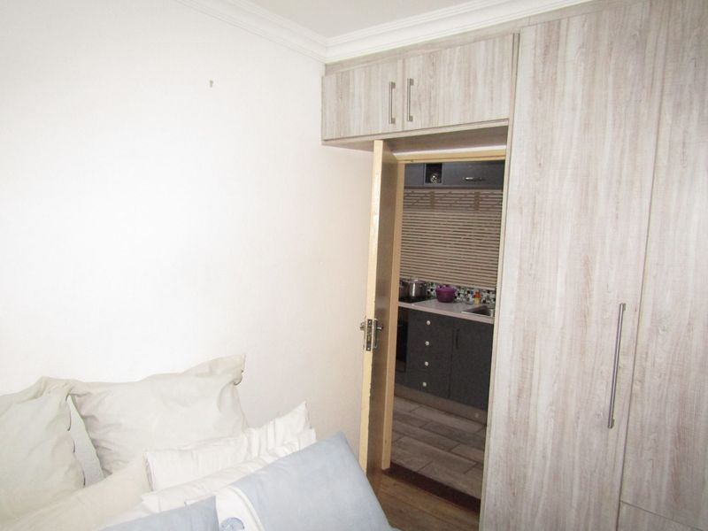Bedroom featuring built-in wood-grain wardrobes with overhead storage, providing direct access to the adjacent kitchen area.
