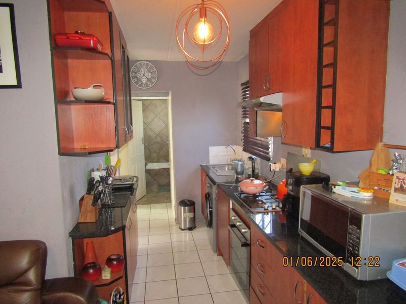 Compact galley-style kitchen featuring wood-finish cabinetry, granite countertops, built-in oven, gas hob, and tiled flooring, with direct access to the bathroom area.