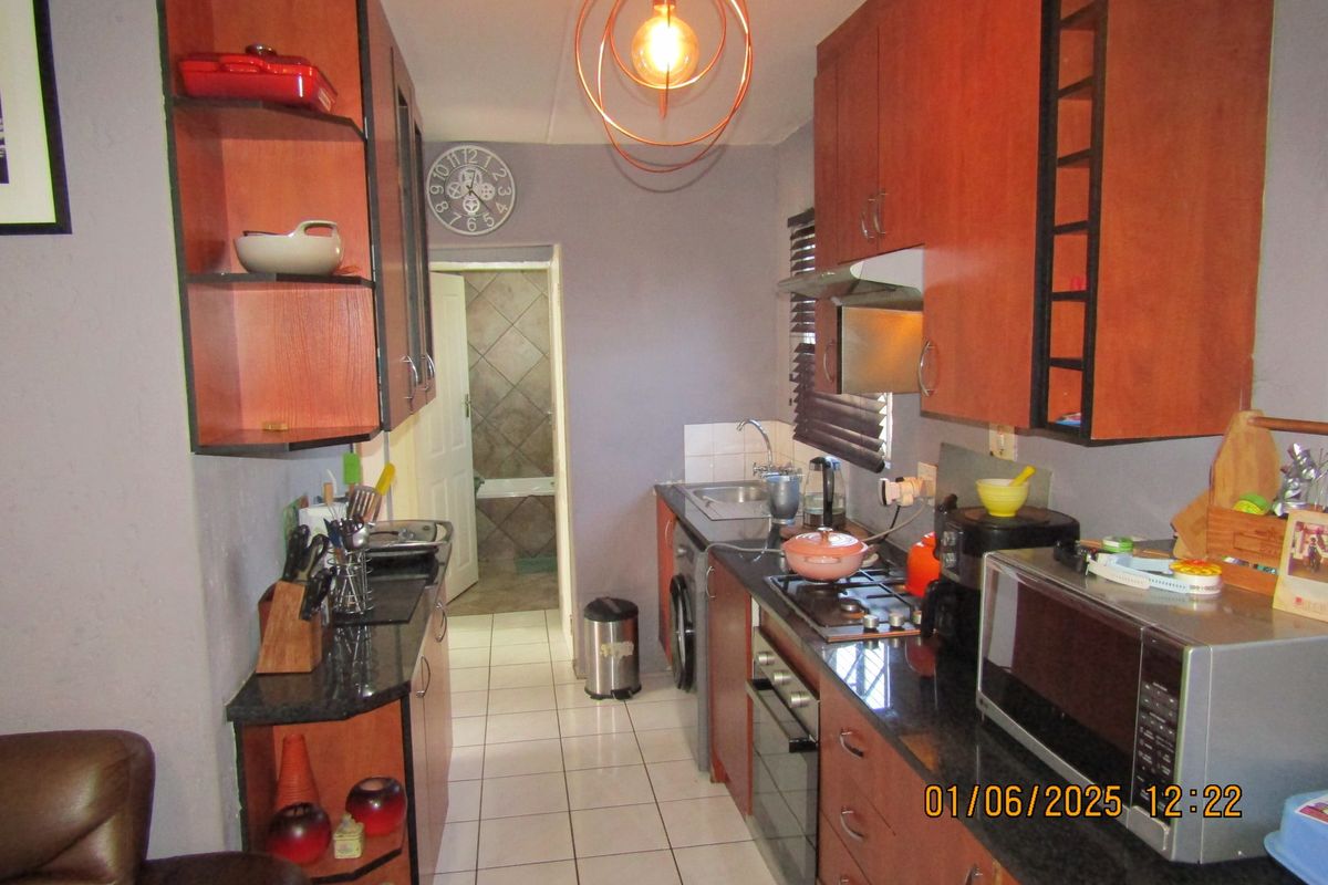 Compact galley-style kitchen featuring wood-finish cabinetry, granite countertops, built-in oven, gas hob, and tiled flooring, with direct access to the bathroom area.