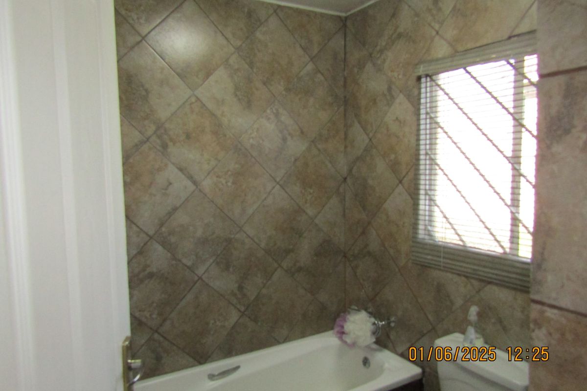 A bathroom featuring a bathtub and tiled wall finishes, including a window with fitted blinds.