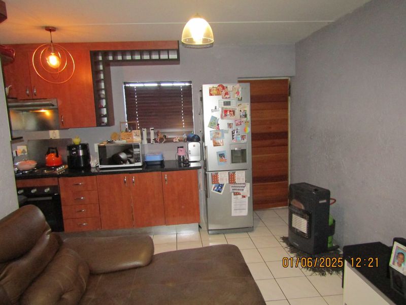Open plan kitchen and living area featuring wooden cabinetry, granite countertops, built-in oven, gas hob, and tiled flooring.