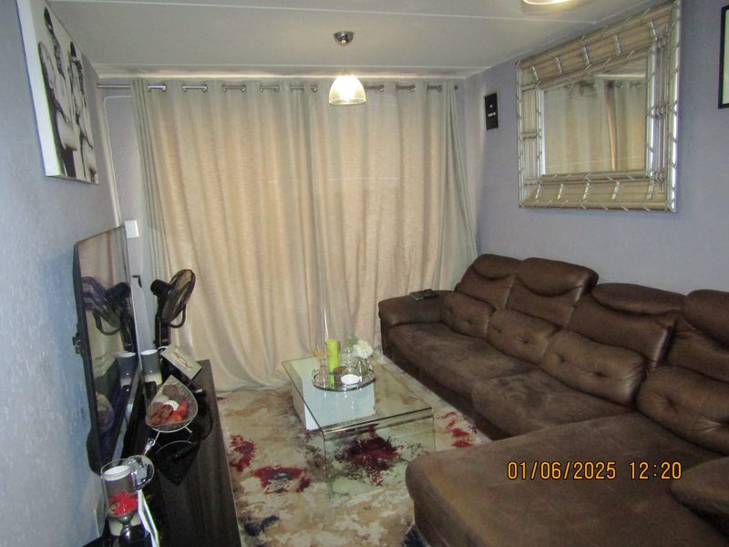 A compact living room featuring neutral wall tones, a large window covered by floor-to-ceiling curtains, and central pendant lighting.