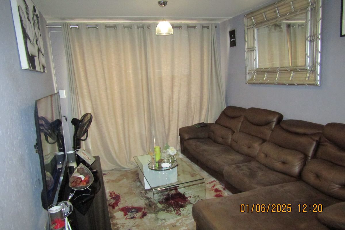 A compact living room featuring neutral wall tones, a large window covered by floor-to-ceiling curtains, and central pendant lighting.