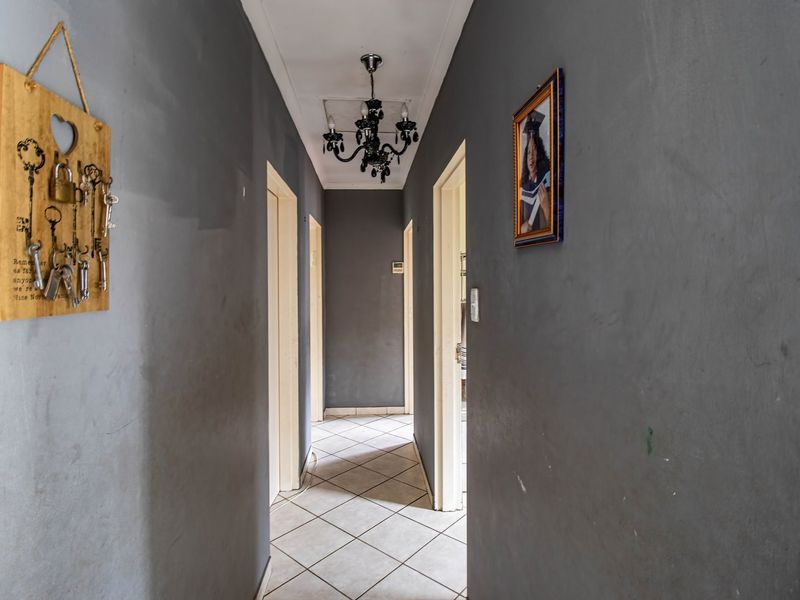 A functional hallway featuring tiled flooring, neutral grey walls, and a central chandelier, providing access to multiple rooms within the townhouse.