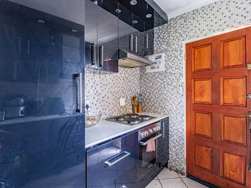 Compact kitchen featuring high-gloss dark cabinetry, built-in oven and hob, mosaic tile backsplash, and a solid wood door.