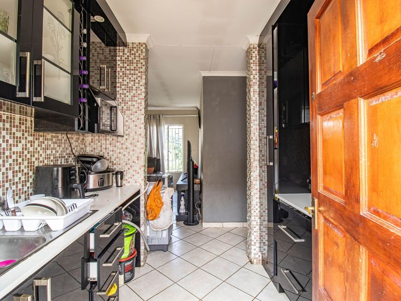 Compact kitchen featuring black built-in cabinetry, mosaic tile backsplash, and tiled flooring, leading into an adjacent living area.