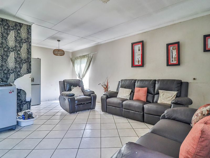 Open plan living area featuring tiled flooring and drop ceiling tiles, currently showing signs of wear including damaged ceiling panels and peeling wallpaper.