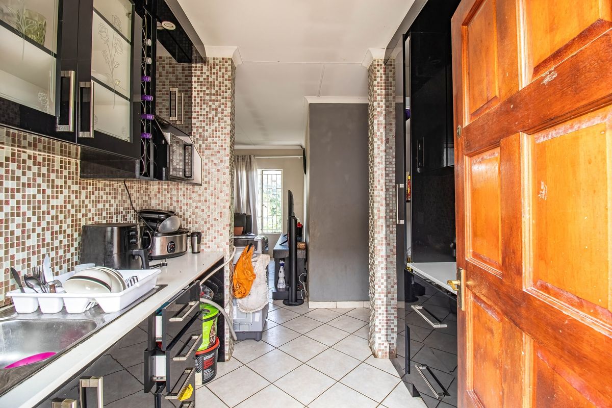 Compact kitchen featuring black built-in cabinetry, mosaic tile backsplash, and tiled flooring, leading into an adjacent living area.