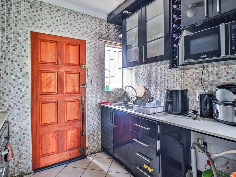 Compact kitchen featuring dark cabinetry, mosaic wall tiling, built-in microwave, and a timber door leading to the exterior.