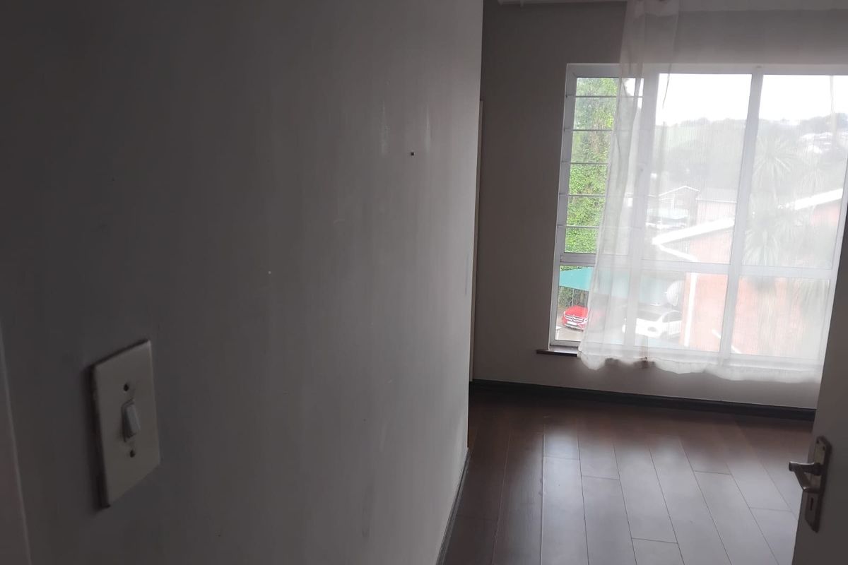 An empty bedroom featuring dark laminate flooring and a large window providing natural light and a view of the surrounding area.