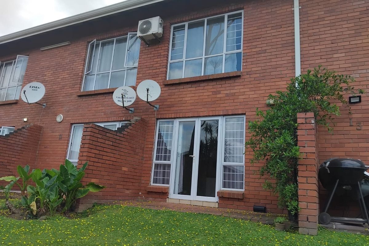 Rear view of a face brick apartment unit featuring aluminium window frames, security bars, and a small private garden area.