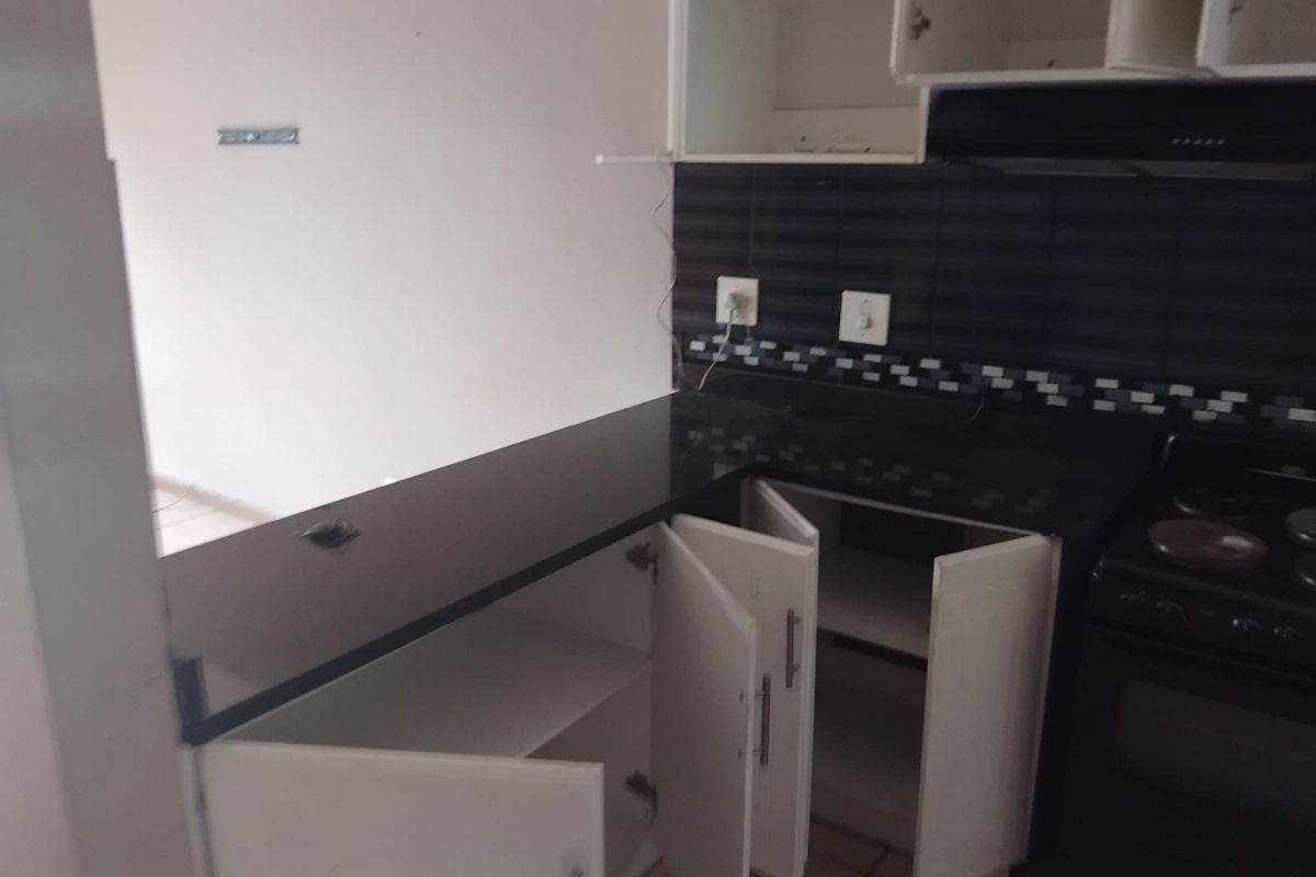 A compact kitchen featuring black countertops, tiled backsplash, and built-in cabinetry, currently in need of minor repairs and cosmetic updates.