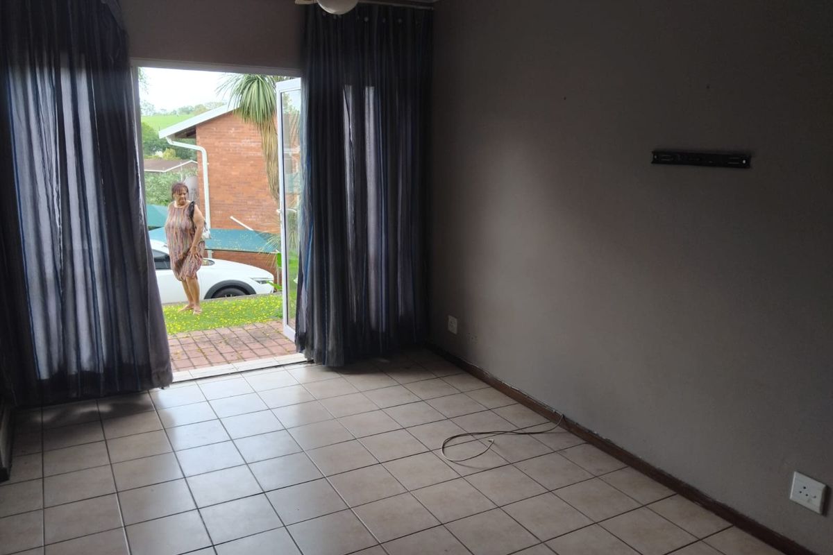 An empty living room featuring tiled flooring, a ceiling fan, and a sliding glass door providing direct access to the exterior.