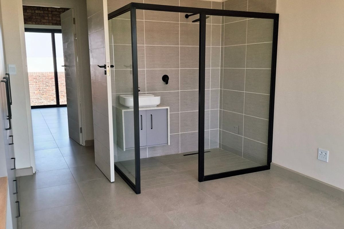 Modern bathroom featuring a sleek glass shower enclosure, wall-mounted vanity with vessel sink, and neutral floor-to-ceiling tiling.