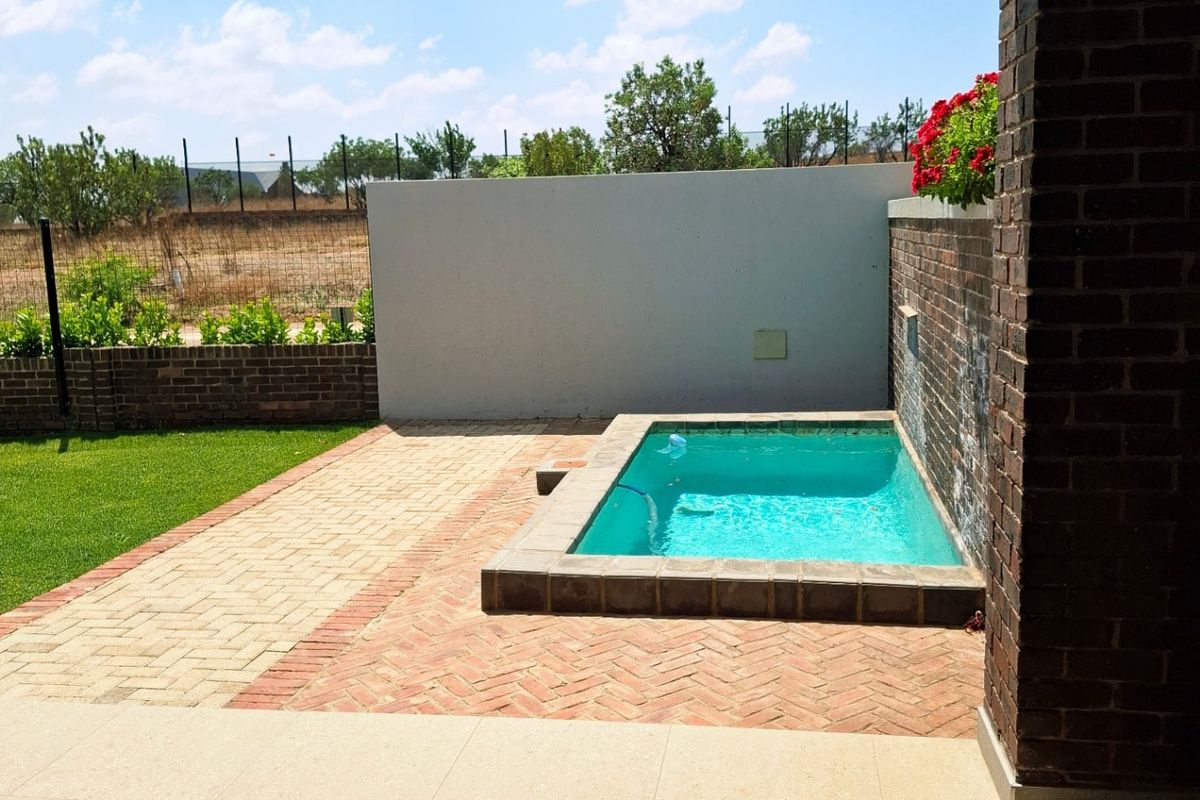 A well-maintained outdoor area featuring a small swimming pool, brick-paved surround, and a covered patio space overlooking the garden.