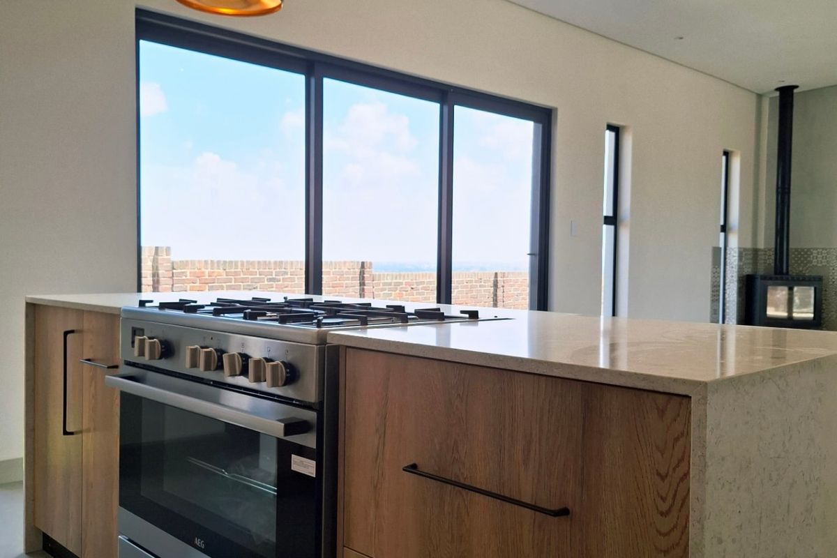 Modern kitchen featuring a central island with stone countertops, wood cabinetry, a gas stove, and pendant lighting, opening to an outdoor area.