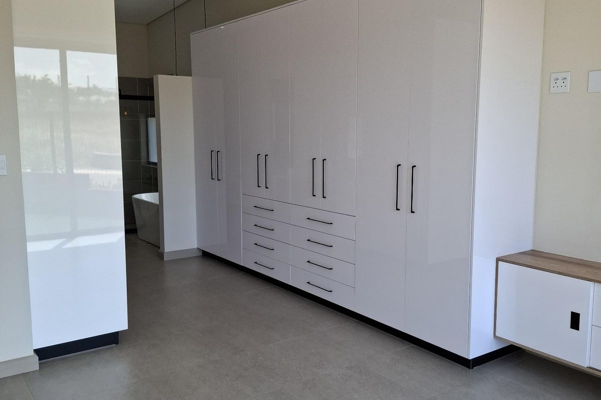 Spacious bedroom featuring modern built-in cupboards, sleek tiled flooring, recessed lighting, and an integrated en-suite bathroom area with a freestanding bathtub.
