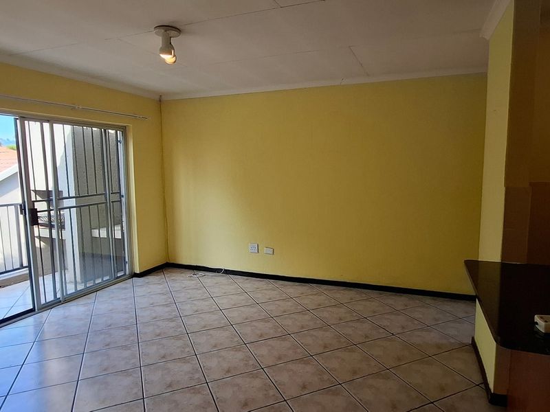An empty open-plan living area featuring tiled floors, a breakfast bar, and a sliding glass door leading to a balcony.