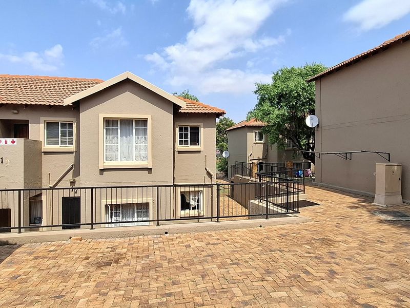 Exterior view of a multi-unit apartment complex featuring paved driveway access, tiled roofing, and metal safety balustrades.