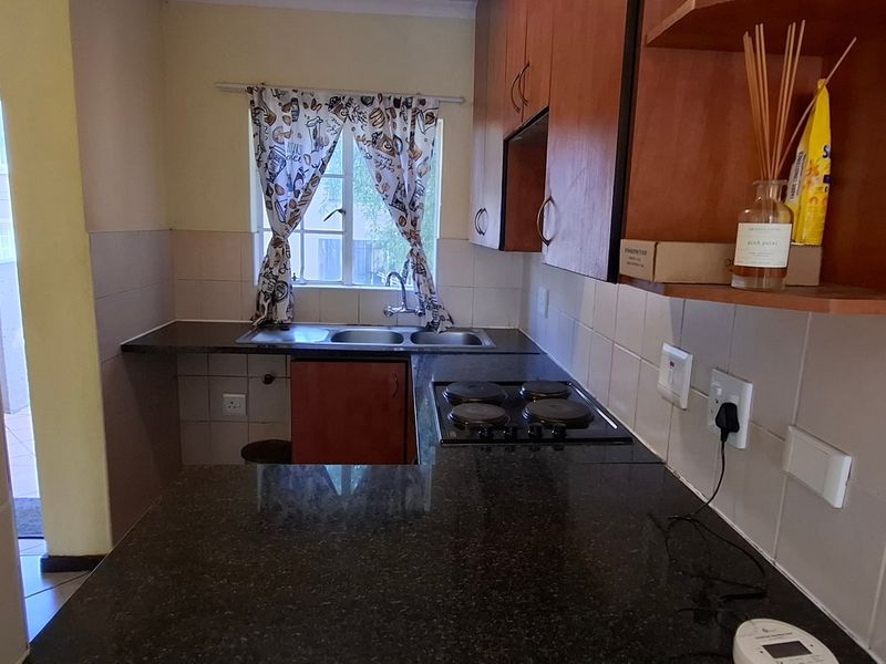A functional kitchen featuring dark granite countertops, built-in wooden cabinetry, an electric hob, and a double basin sink with tiled splashbacks.