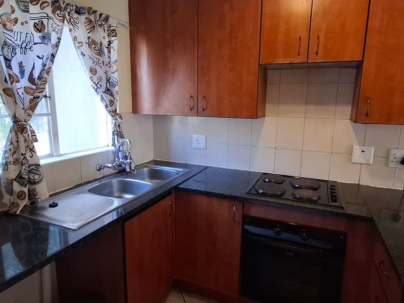 A functional kitchen featuring wooden cabinetry, granite countertops, a built-in oven, electric hob, and a stainless steel double sink with a tiled backsplash.